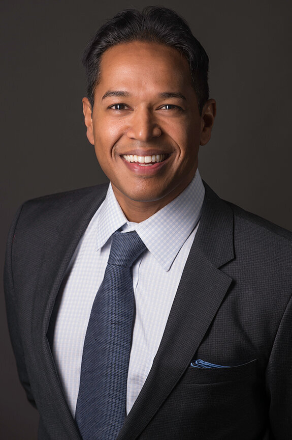 Smiling professional headshot of a man in a navy suit and tie