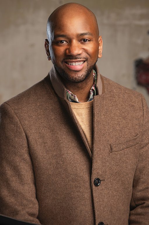 Professional in a gray blazer and maroon shirt against a dramatic dark background